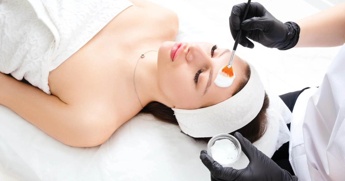 High-angle view of a woman receiving a facial peel, with a technician applying the product using a brush, for Chemical Peels in Glenwood Springs.